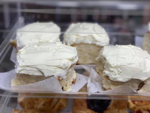 Four frosted pastries displayed in a clear container, featuring a creamy white icing on top.