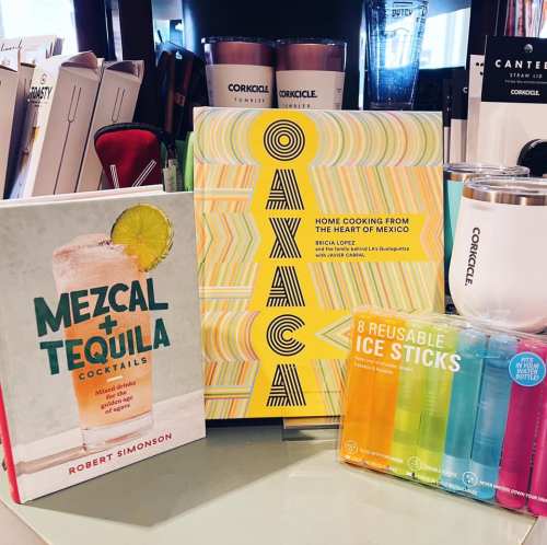 A display of cookbooks and reusable ice sticks, featuring "Mezcal + Tequila Cocktails" and "Oaxaca."