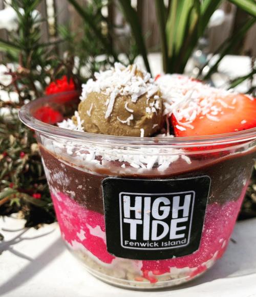 A colorful dessert cup with layers of pink, chocolate, and coconut, topped with strawberries and a scoop of green.