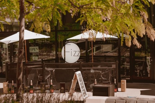 Outdoor seating area of a champagne bar named "Fizz," featuring umbrellas and bottles of champagne.