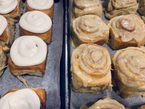 Freshly baked cinnamon rolls with cream cheese frosting, arranged on a baking tray.