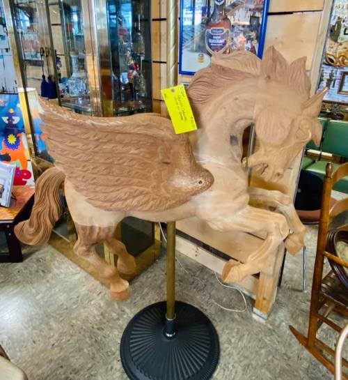 A wooden sculpture of a winged horse, displayed on a stand in a shop, with a price tag attached.