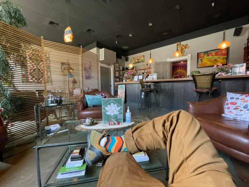 Cozy café interior with a person’s leg and colorful socks resting on a table, surrounded by plants and warm lighting.