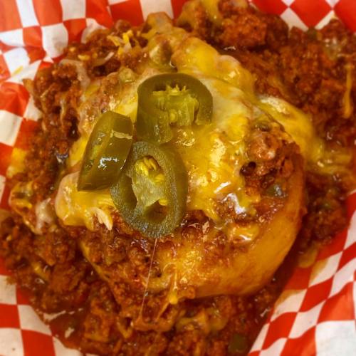 A close-up of a cheesy chili dish topped with jalapeños, served in a red and white checkered paper.