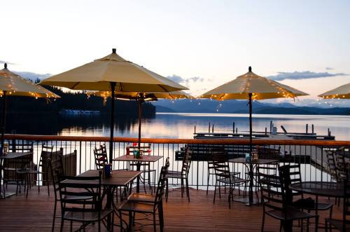 A serene lakeside restaurant deck with yellow umbrellas, twinkling lights, and a calm water view at sunset.