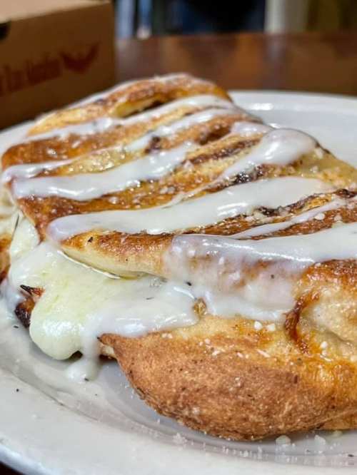 A close-up of a cinnamon roll drizzled with white icing on a white plate.