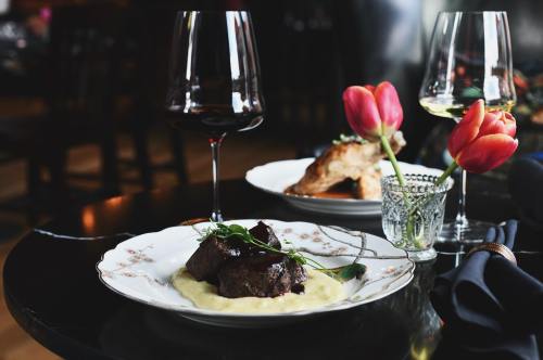 A plate of tender beef on creamy mashed potatoes, accompanied by wine glasses and tulips on a stylish dining table.