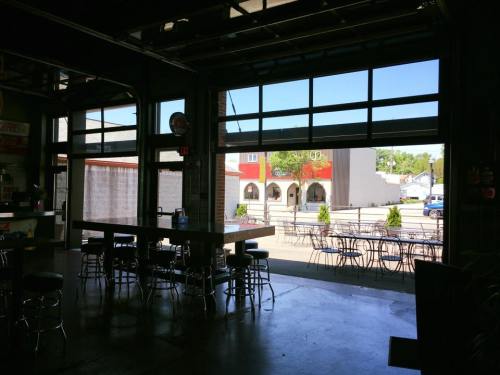 Interior of a cafe with an open garage door, revealing a sunny street and outdoor seating.