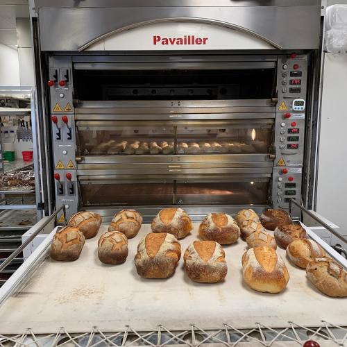 Freshly baked bread loaves cooling on a tray in front of a commercial oven.
