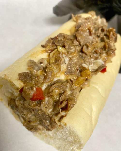 A close-up of a loaded sandwich filled with chopped meat and colorful peppers in a soft hoagie roll.