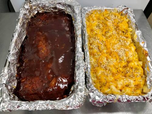 Two foil trays: one with barbecue meat and the other with cheesy pasta topped with breadcrumbs.