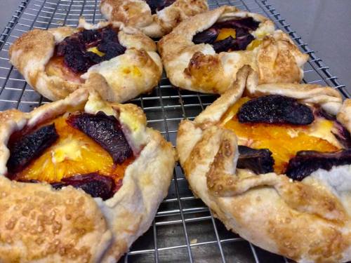 Freshly baked pastries with a golden crust, filled with orange slices and dark fruit, cooling on a wire rack.