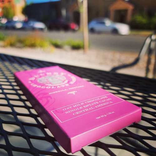 A purple chocolate bar package rests on a table, with a blurred street scene in the background.
