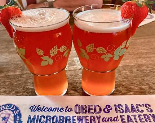 Two glasses of strawberry beer with garnished strawberries, placed on a wooden table with a menu in the background.