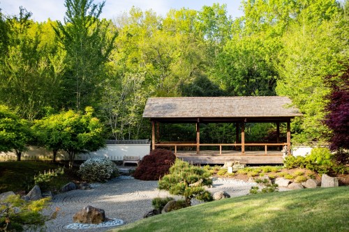 A serene garden with a wooden pavilion surrounded by lush greenery and a stone pathway.