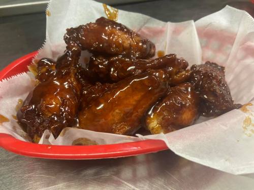 A basket of glazed chicken wings on parchment paper, glistening with a rich, sticky sauce.