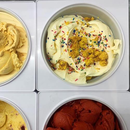 A close-up of ice cream tubs featuring yellow, white, and red flavors, with sprinkles on the white ice cream.