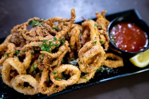 A plate of crispy fried calamari served with marinara sauce and a lemon wedge, garnished with parsley.