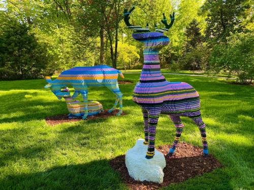 Colorful, striped sculptures of deer made from stacked blocks, set in a lush green park.