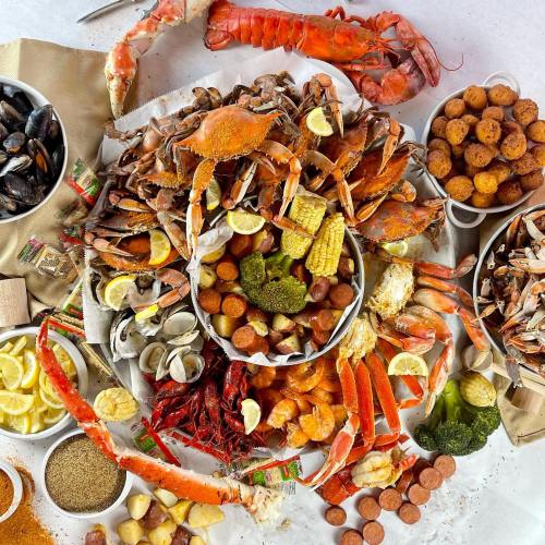 A vibrant seafood spread featuring crabs, shrimp, mussels, corn, potatoes, and various seasonings on a table.
