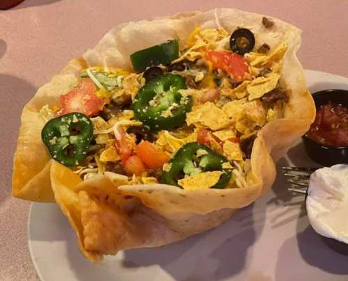 A crispy tortilla bowl filled with beef, cheese, jalapeños, tomatoes, and tortilla chips, served with salsa and sour cream.