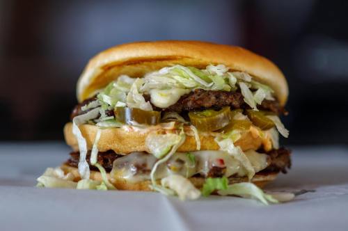 A stacked burger with two patties, lettuce, pickles, and sauce, served on a soft bun.