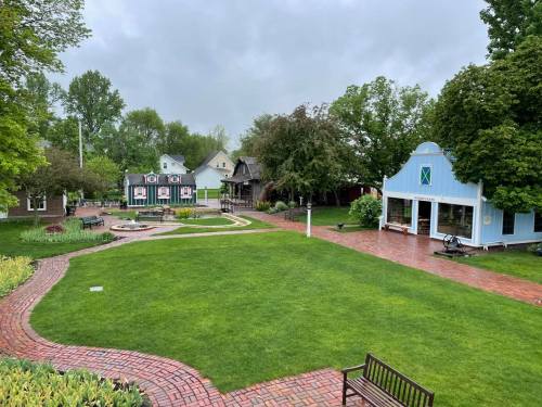 A lush green park with brick pathways, colorful buildings, and a cloudy sky in the background.