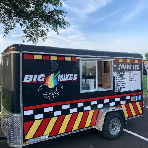 A colorful food trailer named "Big Mike's" serving shave ice, featuring various flavor options on the side.