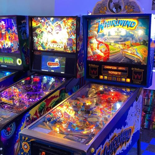 Two colorful pinball machines in an arcade, featuring vibrant artwork and illuminated playfields.