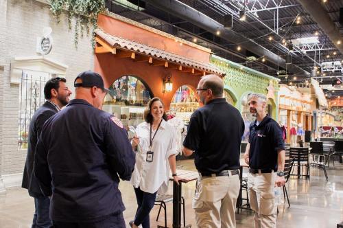 A group of people chatting in a vibrant indoor market with colorful decor and seating areas.