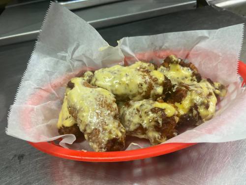 A red basket filled with cheesy, saucy chicken wings on a bed of parchment paper.