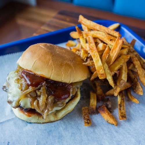 A juicy burger with melted cheese and caramelized onions, served with a side of crispy French fries on a blue tray.