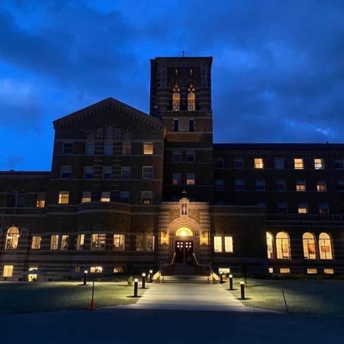 Historic building illuminated at dusk, featuring a tall clock tower and glowing windows against a darkening sky.