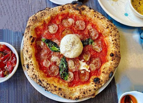 A freshly baked pizza topped with pepperoni, basil, and a creamy burrata in the center, served on a white plate.