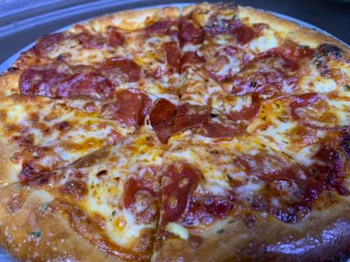 A freshly baked pepperoni pizza with melted cheese, sliced into eight pieces on a silver tray.