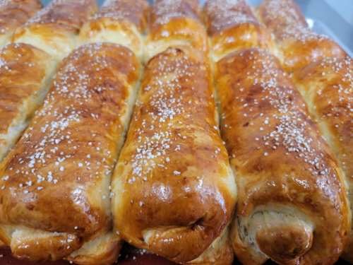 Freshly baked golden-brown bread rolls, topped with coarse salt, arranged in a row.