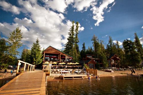 A lakeside scene featuring a wooden dock, a restaurant, and people enjoying the water surrounded by tall trees and blue skies.