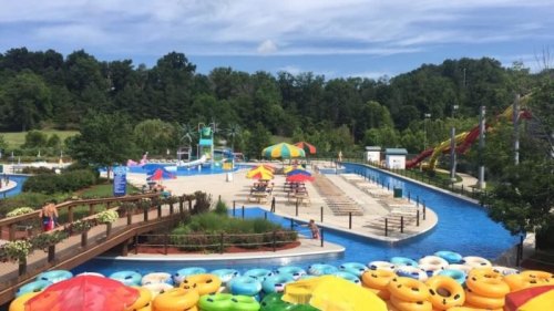 A vibrant water park scene with colorful tubes, slides, and lounge chairs under a blue sky.