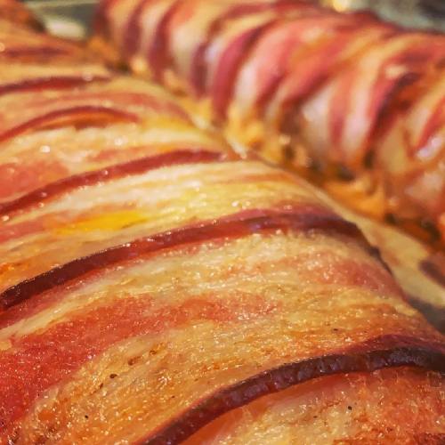 Close-up of two meatloafs wrapped in crispy bacon, showcasing their golden-brown, glistening layers.