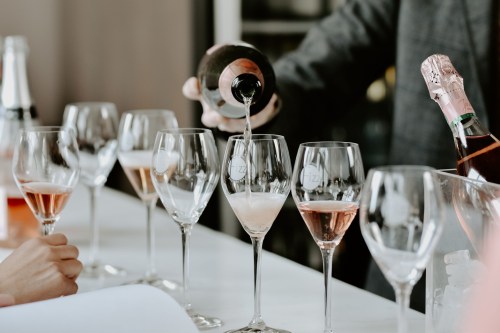 A person pours sparkling wine into elegant glasses at a bar, with several filled glasses in the foreground.