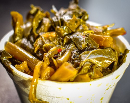 A close-up of a cup filled with cooked greens, featuring dark leafy vegetables and stems, glistening with moisture.
