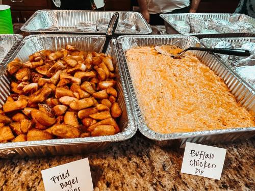 Two trays of food: one with fried bagel bites and another with buffalo chicken dip, both labeled on a countertop.
