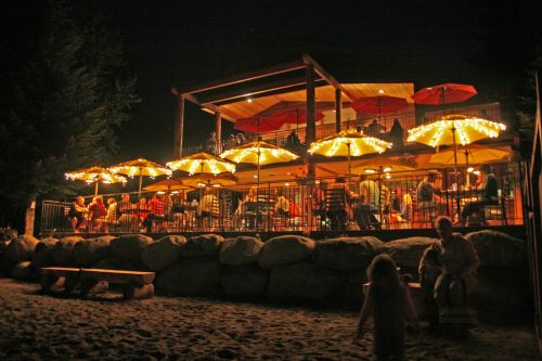 A lively outdoor restaurant at night, featuring illuminated umbrellas and diners enjoying the ambiance by the beach.