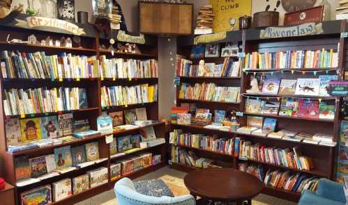 A cozy library corner with bookshelves labeled Gryffindor, Slytherin, Hufflepuff, and Ravenclaw, filled with colorful books.