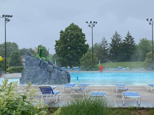A misty pool area featuring a dragon statue on a rock, surrounded by empty lounge chairs and trees in the background.