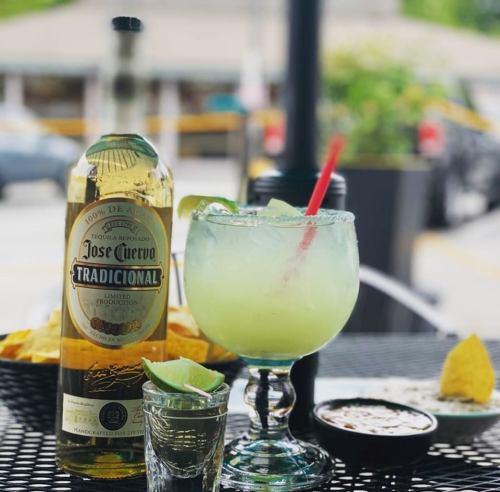 A refreshing margarita with lime, a shot of tequila, and tortilla chips on a table outdoors.