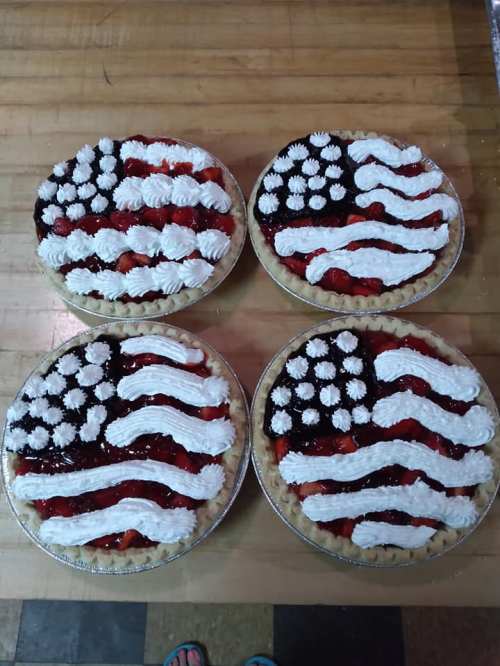 Four pies decorated to resemble the American flag, featuring red, white, and blue toppings on a crust.