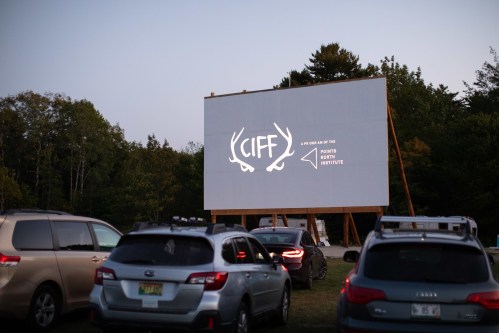 A large outdoor screen displays the CIFF logo, surrounded by parked cars in a wooded area at dusk.