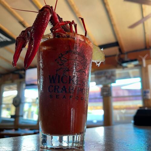 A glass of Bloody Mary garnished with a crawfish and lime, set on a wooden table in a seafood restaurant.