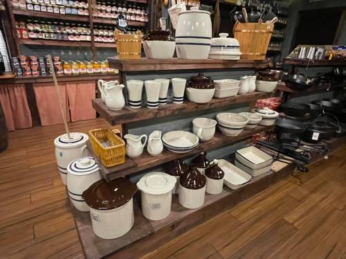 A display of various ceramic kitchenware, including bowls, pitchers, and storage containers, arranged on wooden shelves.